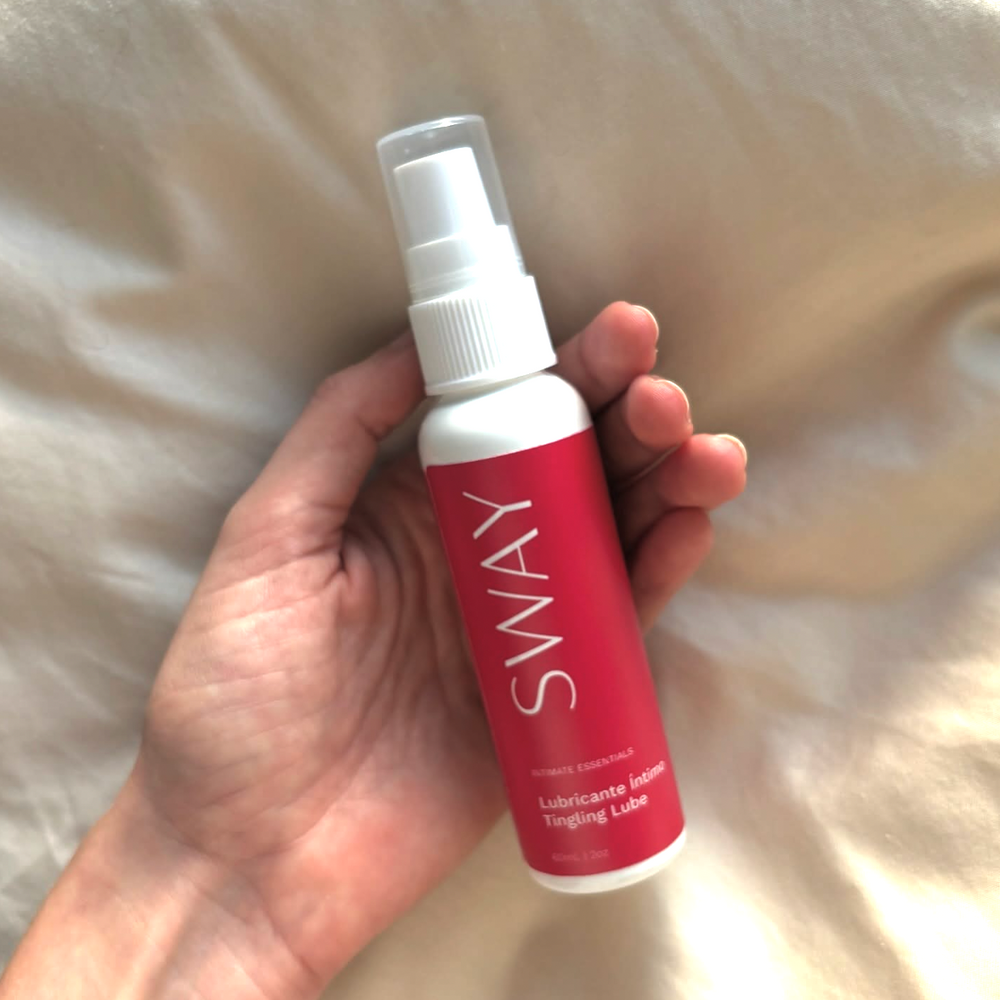 Hand holding a Sway lubricant bottle against a neutral background